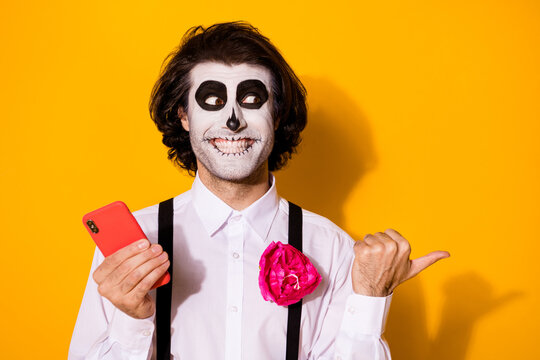 Close-up portrait of his he nice handsome spooky cheerful glad guy using device app 5g smm showing copy space advice calavera look idea isolated bright vivid shine vibrant yellow color background