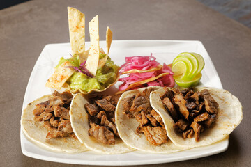 Angus beef tacos with pickled purple onion accompanied by guacamole and lemon.