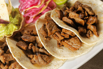 Angus beef tacos with pickled purple onion accompanied by guacamole and lemon.