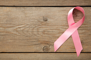 Pink breast cancer ribbon on grey wooden background.