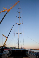 Placing a mast on a super sailing yacht at the harbor. Ship building industry. Shipyard. Building superyachts. Rigging.  Crane. 