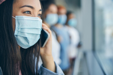 Young beautiful lady in protective mask talking on mobile phone in front of glass window