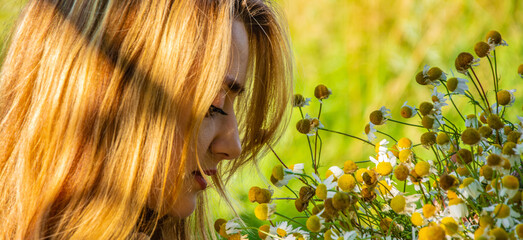 Naklejka premium Young beautiful smiling woman smells bouquet of yellow field flowers, against green summer fiel.
