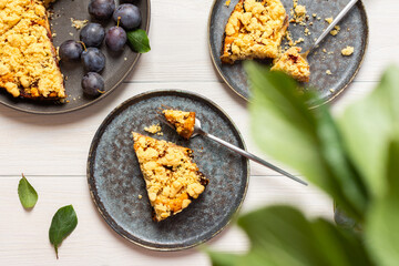 Delicious juicy dessert on a white wooden background, portions of plum pie in a plate with a fork