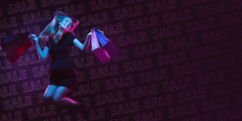 Jumping high. Portrait of young beautiful woman in neon light on dark studio backgound with lettering SALE. Human emotions, black friday, cyber monday, purchases, sales, finance. Copyspace.