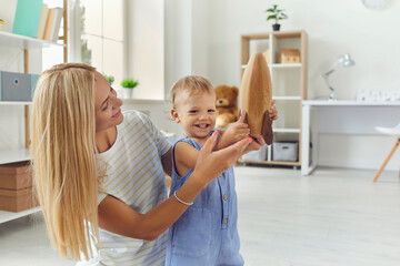 Happy mother with smiling baby boy playing together with wooden rocket at home