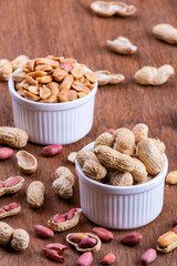 Peanuts in a white bowl rests on an old wooden table.