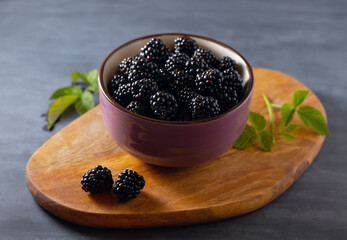 Fresh blackberries in a bowl on a rustic board on the table. Close-up.