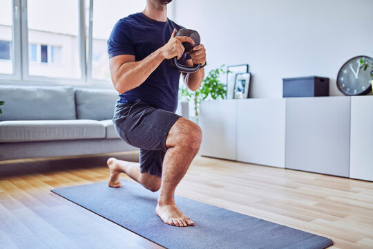 Home workout, closeup of athletic man doing lunges with kettlebell at home