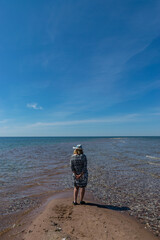 a female figure on the seashore, a beautiful blue sky and a pebble beach