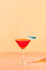 Vacation red cocktail in martini glass with blue paper plane  on yellow background