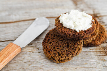 Small round rye toasts with cream cheese. Old wooden background, selective focus, close up.