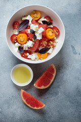 Bowl of grapefruit, feta cheese and tomato salad over light-blue stone background, view from above, studio shot
