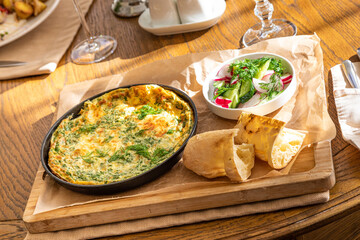 Omelet in a frying pan with parsley and dill. Serve with fresh bread and fresh vegetables.