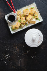 White plate with roasted chunks of tofu cheese, top view on a dark brown stone background, vertical shot with space