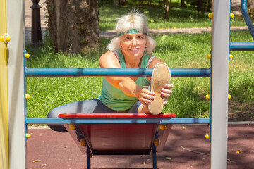 Obraz premium Slender elderly woman with gray hair conducts individual fitness classes on a simulator in a city park. Close-up