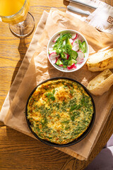 Omelet in a frying pan with parsley and dill. Serve with fresh bread and fresh vegetables.