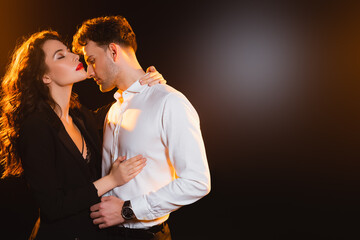 curly woman in jacket hugging man in shirt on black