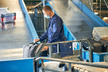 Man in coverall checking a tag on passengers luggage