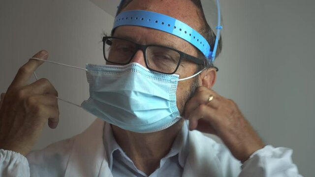 Portrait of a tired handsome male doctor taking off the surgical face mask looking at the camera and smiling in the hospital during the Covid-19 Coronavirus pandemic.