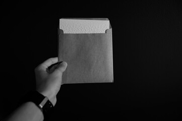 Man with watch holding blank white letter in envelope in black and white