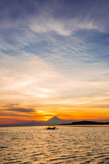 Sunset over a volcano and the ocean with a small traditional boat silhouette