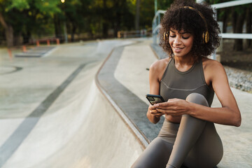 Image of african american sportswoman using cellphone and headphones