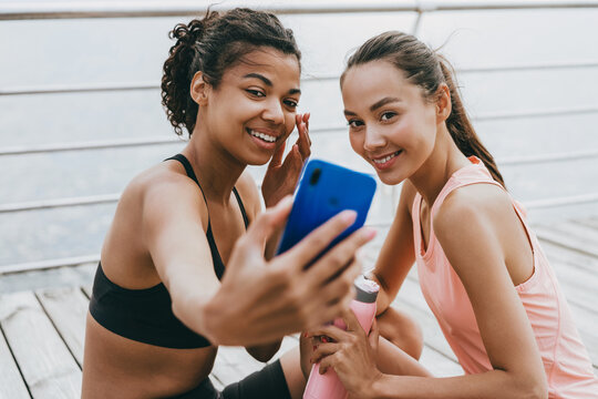 Image of happy multinational sportswomen taking selfie on cellphone while sitting