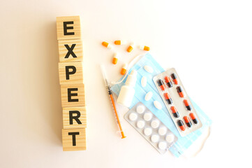 The words EXPERT is made of wooden cubes on a white background with medical drugs and medical mask. Medical concept.
