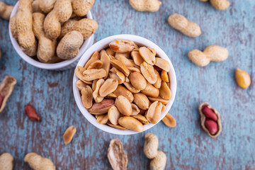 Peanuts in a white bowl rests on an old wooden table.
