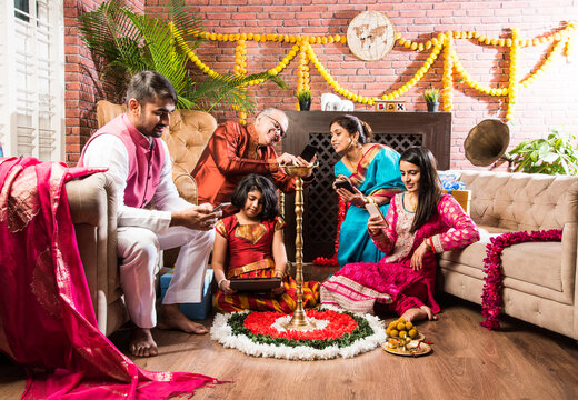 Happy Indian Family Celebrating Ganesh Festival Or Chaturthi - Welcoming Or Performing Pooja And Eating Sweets In Traditional Wear At Home Decorated With Marigold Flowers