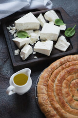 Feta cheese on a wooden serving tray with greek traditional spanakopita pie in the foreground, vertical shot, selective focus