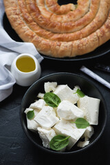 Bowl with feta cheese and spiral spanakopita pie in the background, vertical shot on a black stone surface, elevated view