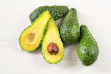Close-up photo of avocados cut to half, brown seeds visible, with more avocados on white wooden background. Fresh sliced avocado.Vegetarian food concept.