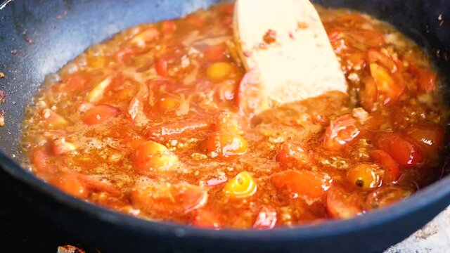 Close-up of cooking tomatoes and pork chops in red curry paste in pan (Nam Prik Ong). Famous food in the north of Thailand.