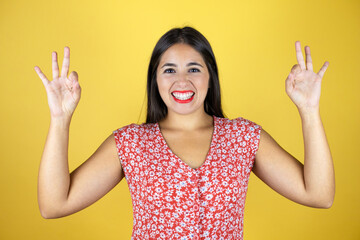 Young beautiful woman over isolated yellow background doing ok sign with fingers and smiling, excellent symbol