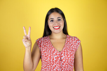 Young beautiful woman over isolated yellow background showing and pointing up with fingers number two while smiling confident and happy