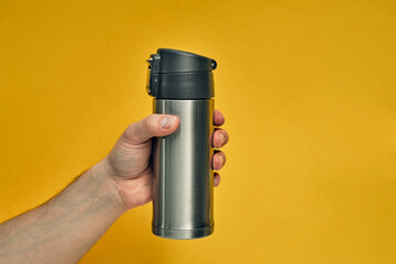 Metal mug thermos in hand on a colored background. Hot drinks on the go. Thermo mug.