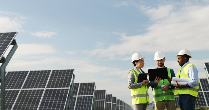 Portrait of electrician engineers in safety helmet and uniform checking solar panels. Group of three engineers at solar station.