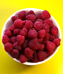 Raspberries in a white plate on a yellow background.