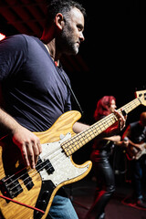 Obraz premium Caucasian Man is Performing on the Stage with Band. Handsome Male Person is Playing on Bass Guitar at Concert.