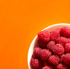 Raspberry berries in a white plate on an orange background.