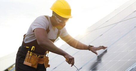 Portrait of african american engineer in safety helmet and uniform at solar power station...