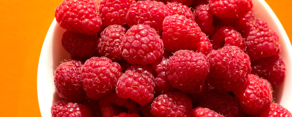 Raspberry berries in a white plate on an orange background.
