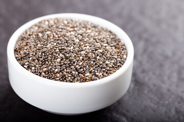 Chia seeds in bowl on black stone background.