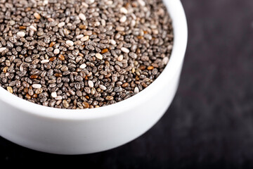 Chia seeds in bowl on black stone background.