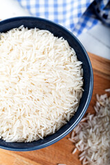 Uncooked basmati rice in a ceramic bowl on wooden background