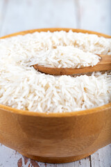 Wooden bowl full of basmati rice on wooden background.