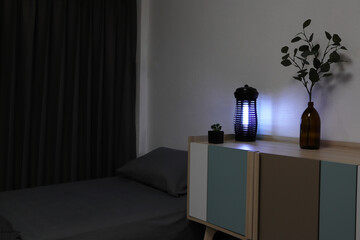 the insects mosquito electric blue light killer lamp is put on the wooden table in the dark bedroom...