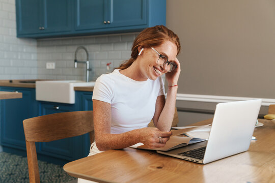 Image of smiling ginger woman in earphones working with laptop